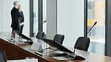 Microphones and digital displays line a polished wooden table in a modern corporate boardroom.