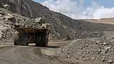 A large yellow mining truck transports rock through a sprawling open-pit quarry.
