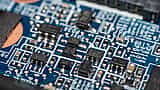A close-up macro view of a blue electronic circuit board with various surface-mounted components.