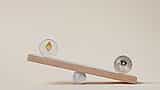 A silver Ethereum coin and a silver Bitcoin coin balancing on opposite ends of a wooden seesaw against a beige background.
