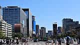 People cross a street lined with modern commercial high-rises in a sunny business district of Seoul, South Korea.