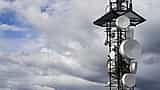 A tall telecommunications tower equipped with large white satellite dishes stands against a cloudy sky.