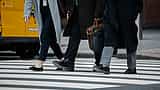A crop of professionals carrying briefcases as they cross a downtown city street.