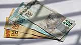 Brazilian Real banknotes of various denominations are fanned out under slatted sunlight.