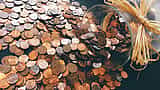A glass jar lies on its side, spilling a large mound of copper pennies onto a flat surface.