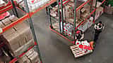 A high-angle view of workers organizing inventory on pallets in a vast, well-stocked industrial warehouse.