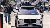 A white Waymo self-driving vehicle with roof-mounted sensors navigates a city street.