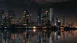 The modern high-rises of the Mumbai skyline glow at night, reflecting off the dark waters below.