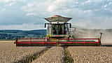 A massive combine harvester cutting through a golden wheat field with grain piled high in its hopper.
