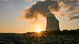 The sun bursts over the horizon in front of two nuclear power plant cooling towers.