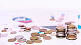 A neat stack of coins resting on printed financial charts and data.