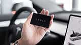 A hand holds a black Tesla key card inside the modern interior of a vehicle.