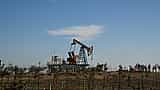 A solitary oil pump jack operates in a dry, sparse landscape under a clear sky.