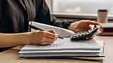 A person's hands use a calculator over a stack of financial documents and charts.