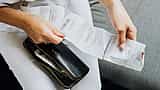 Close-up of a person's hands reviewing multiple store receipts pulled from a black wallet.