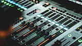 Close-up of a modern audio mixing console with illuminated sliders and dials.