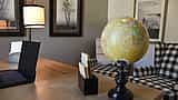 A world globe, a laptop, and wooden calendar blocks sit on a desk in a warm, modern office setting.