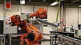 A yellow industrial robotic arm operates within a modern manufacturing or laboratory setting.