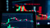 A digital trading chart is displayed on a screen in sharp focus, with a larger, brightly lit chart blurred in the background.