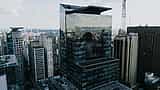 A tall, modern glass skyscraper reflects the dense urban skyline of São Paulo.