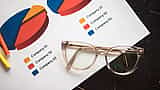 Transparent eyeglasses rest on a printed document displaying colorful pie charts and a legend detailing company allocations.