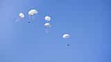 Multiple white parachutes safely lowering cargo boxes through a clear blue sky.