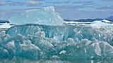 A large, textured blue iceberg floats in the water with its submerged layers visible beneath the surface.