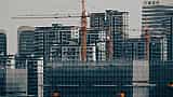 Multiple construction cranes tower over unfinished high-rise buildings surrounded by scaffolding in a Chinese city.