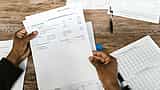 A person's hands hold up a financial statement over a wooden desk with a tax form resting nearby.