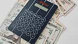 A black digital calculator rests on top of a scattered pile of U.S. dollar bills.