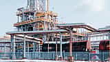 An oil refinery complex with metal pipelines stands behind black transport tanker wagons.