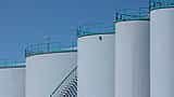 Large, white industrial oil storage tanks stand under a clear blue sky.
