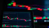 A digital screen displays a cryptocurrency trading chart with prominent red candlestick patterns indicating a market decline.