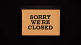 A framed sign reading 'Sorry we're closed' against a dark background.