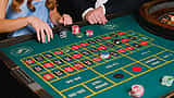 People place stacks of chips on a green casino roulette table.