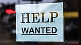 A red and white Help Wanted sign taped to the inside of a glass storefront window.