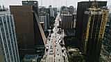 An aerial daytime view of Paulista Avenue in São Paulo, Brazil, showing heavy traffic and modern corporate skyscrapers.