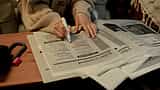 A person uses a pink marker to highlight job listings in the classifieds section of a newspaper.