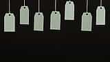 Multiple blank cardboard price tags hang from strings against a dark background.