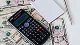 A black scientific calculator and a blank notepad sit on a scattered pile of US dollar bills.