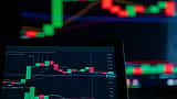 A close-up of a digital monitor displaying a financial candlestick chart with red downward trends.