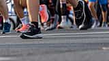 A close-up view of the feet and legs of multiple marathon runners moving along a paved road.
