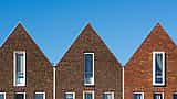 A row of contemporary brick houses with uniform pitched roofs under a bright blue sky.