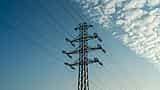 A tall electrical transmission tower stands against a bright blue sky with scattered clouds.