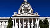 The white facade and dome of the California State Capitol building against a clear blue sky.