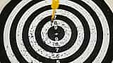 A single dart rests in the bullseye of a black and white target board.