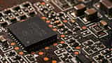 A moody, extreme close-up of a black microchip mounted on an intricate, shadowed circuit board.