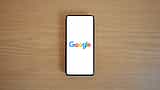 A smartphone displaying the Google logo lies flat on a light wooden surface.