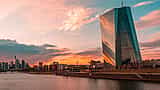 The modern glass facade of the European Central Bank headquarters in Frankfurt reflecting a vibrant sunset.