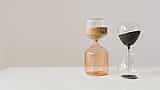 Two modern glass hourglasses with flowing sand sit side-by-side on a white surface.